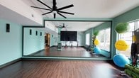 Located at 400 South Greene St in Greenville, NC, this single-floor fitness and recreation facility is designed to support a wide range of physical activities in a vibrant, well-appointed environment. The space is defined by its signature teal and mint green color palette, warm hardwood-style flooring, and soaring ceilings equipped with large industrial ceiling fans that promote airflow throughout the open layout.

The cycling studio is a standout feature, housing a row of red stationary bikes positioned before a bold, large-scale typographic mural that energizes the room. A sizable mounted flat-screen display faces the riders, supporting guided workout sessions. Full-length mirrors line the walls, amplifying the sense of space and allowing participants to monitor their form.

Adjacent to the cycling area is a versatile exercise zone stocked with an extensive array of fitness equipment, including medicine balls, stability balls, resistance bands, foam rollers, and a dumbbell rack. Large windows along the exterior wall flood this area with natural light and provide outdoor views, creating an open and inviting atmosphere.

A separate recreation room, visible through an open doorway, features a pool table beneath a stylish pendant light, offering a social space for leisure and relaxation. Together, these areas create a comprehensive facility that balances active fitness with casual recreation.
