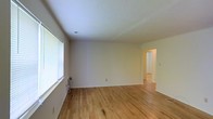 Located at 2 Dutton Dr in Matawan, NJ, this single-floor space presents a straightforward and functional layout with a clean, move-in-ready aesthetic. The main living area is finished with light-toned hardwood flooring that runs throughout, lending warmth and continuity to the space. Neutral white walls create a bright, open atmosphere that serves as a versatile backdrop for a variety of interior styles.

A large window fitted with horizontal blinds lines one wall of the main room, allowing ample natural light to fill the space while offering the option for privacy. A wall-mounted heating unit is positioned beneath the window, providing a practical heating solution. Recessed lighting in the ceiling adds to the overall brightness of the room.

An open doorway visible from the main area leads into an adjacent room, suggesting a connected and accessible floor plan. The consistent hardwood flooring continues into this adjoining space, reinforcing the cohesive design throughout. The layout appears well-suited for comfortable everyday living, with a simple and uncluttered design that emphasizes functionality and ease of use.