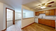 Located at 3223 North Street in East Troy, WI, this single-floor, one-bedroom, one-bathroom unit offers a practical and well-organized layout. The combined kitchen and living area serves as the heart of the space, featuring warm wood-toned cabinetry, a double sink, a dishwasher, a range, and a full-size refrigerator. A half-wall pass-through opens the kitchen to the living area, creating an airy, connected feel. Hardwood-style flooring runs throughout the main living areas, complemented by ceiling fans that add both function and character. Natural light filters in through windows in the living area and bedroom, providing pleasant outdoor views. The carpeted bedroom offers a comfortable retreat with a ceiling fan and access to closet space, while four closets throughout the unit provide generous storage. An additional den presents flexible space ideal for a home office or secondary sitting area. The bathroom features hardwood-style flooring, a wood-trimmed vanity with storage below, and a clean, neutral palette. A hallway connects the private areas of the unit, and baseboard heating is present throughout. The overall ambiance is cozy, functional, and well-suited for comfortable everyday living.