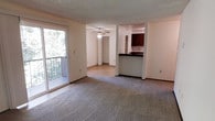 Located at 4519 SW 321st in Federal Way, Washington, this single-floor unit offers a thoughtfully designed layout that maximizes both comfort and functionality. The open living area is finished with plush carpeting and features a ceiling fan, providing a comfortable and relaxed atmosphere. A sliding glass door leads directly to a private balcony, where views of surrounding greenery bring natural light deep into the living space.

The kitchen is positioned adjacent to the living area and is defined by a raised breakfast bar counter, offering a casual dining option as well as a natural division between spaces. Dark-toned cabinetry provides ample storage, and the kitchen's open-pass design maintains a sense of openness throughout. A hallway connects the living spaces to the remainder of the unit, with a bi-fold door visible along the corridor suggesting additional storage or utility access.

Throughout the unit, neutral wall tones and a textured ceiling contribute to a clean, understated aesthetic. The layout flows naturally from the living area toward the kitchen and private rooms, creating an intuitive and easy-to-navigate floor plan. The presence of natural greenery visible from the balcony adds a serene, nature-connected quality to the overall ambiance of this Federal Way residence.