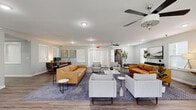 Located in Springdale, Arkansas, this single-floor space combines an open-concept living room and kitchen into a cohesive, functional layout. The living area is generously proportioned, featuring light gray walls, recessed lighting, and wood-look plank flooring that runs continuously throughout. Ceiling fans with contemporary fixtures are positioned across the space, promoting airflow and comfort. Multiple windows fitted with white plantation shutters allow natural light to fill the room while maintaining privacy. A set of glass-paned French doors provides an additional connection to the outdoors. The living area accommodates multiple seating arrangements, reflecting its versatile, open design.

The kitchen is well-equipped and thoughtfully laid out, showcasing white shaker-style cabinetry paired with granite-look countertops. Black appliances, including a range, refrigerator, and microwave, provide a striking contrast against the light cabinetry. A peninsula with an undermount sink and bar seating extends into the space, offering both functionality and a casual dining option. A window above the sink introduces natural light. The consistent wood-look flooring, neutral color palette, and modern fixtures create a unified, welcoming ambiance throughout the entire space.
