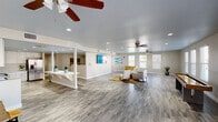 Located at 3311 W Dunlap Ave in Phoenix, Arizona, this single-floor community space offers a thoughtfully designed, open-concept layout that seamlessly connects its key functional areas. Throughout the space, wood-look luxury vinyl flooring provides a cohesive and contemporary aesthetic, complemented by recessed lighting and ceiling fans that ensure comfort in the Arizona climate.

The expansive main area flows between a fully equipped kitchen, a relaxed lounge zone, and a dedicated game room. The kitchen is outfitted with stainless steel appliances — including a range, microwave, dishwasher, and refrigerator — alongside crisp white cabinetry that extends to the ceiling for ample storage. A long white breakfast bar with barstool seating serves as a natural divider between the kitchen and the open common area, offering a casual gathering spot.

The lounge area provides comfortable seating arranged around a woven area rug, creating an inviting setting for socializing. Large windows dressed with white blinds line the walls of the game room, flooding the space with natural light while offering views of the surrounding area. The game room features a foosball table and a shuffleboard table, making it an ideal space for recreation and entertainment. The neutral color palette throughout lends the entire space a clean, modern, and welcoming atmosphere.