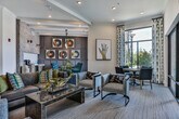 Located along Atlanta Student Movement Boulevard in Atlanta, GA, this single-floor community amenity space is designed with a contemporary aesthetic that balances comfort and sophistication. The open-plan layout connects a generous lounge area with a formal dining zone, creating a versatile gathering environment flooded with natural light from large, floor-to-ceiling windows and glass doors that frame views of the surrounding greenery.

The lounge area is anchored by plush leather and upholstered seating arranged around a substantial stone-topped coffee table, with a wall-mounted flat-screen TV set within a striking striped accent wall feature. Pendant lighting and recessed fixtures provide layered illumination throughout. A glass-walled room divider separates a secondary lounge or meeting area, offering a more private setting without sacrificing visual openness.

The dining area is a standout zone, furnished with a rich wood table surrounded by tufted teal velvet chairs. A dark paneled accent wall serves as a dramatic backdrop for a curated gallery of vinyl record-inspired artwork, complemented by a built-in wet bar with granite countertops and a beverage refrigerator. The combination of tile flooring, plush carpeting, and carefully selected décor gives the overall space a refined, hospitality-inspired character.