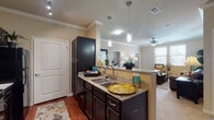 This single-floor residence offers a thoughtfully designed open-concept layout that connects the kitchen, dining, and living areas seamlessly. The kitchen is appointed with dark espresso cabinetry, granite countertops, a peninsula with bar seating, pendant lighting, track lighting, black appliances, and hardwood flooring that extends toward the entryway.

Adjacent to the kitchen, the dining area accommodates a round table and features crown molding and a large decorative mirror. The living room offers carpeted flooring, crown molding, a ceiling fan, and natural light from a window with exterior views.

The primary bedroom is carpeted and includes a ceiling fan, while a secondary bedroom features a window and dresser space. A dedicated office or flex room provides additional carpeted space with a ceiling fan, suitable for a home workspace. The primary bathroom includes dark cabinetry with granite counters, hardwood flooring, and direct access to a walk-in closet with built-in shelving.

An in-unit laundry area houses a full-size washer and dryer with overhead shelving. Crown molding, consistent neutral tones, and cohesive dark wood finishes throughout contribute to a polished, unified aesthetic.