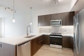 Located at 1500 Westbranch Drive in McLean, VA, this modern one-bedroom, one-bathroom residence offers a thoughtfully designed open-concept layout with clean lines and contemporary finishes. Light wood-tone flooring flows throughout, complementing the bright, neutral palette of the space.

The kitchen is a standout feature, showcasing rich dark wood cabinetry that reaches the ceiling, a textured tile backsplash, and a suite of stainless steel appliances including a range, microwave, dishwasher, and side-by-side refrigerator. A sleek peninsula with a white quartz countertop and pendant lighting above serves as a natural transition into the combined dining and living area, which benefits from large windows that invite natural light and outdoor views.

The bedroom is a calm, well-proportioned retreat with light wood flooring and a generous walk-in closet equipped with built-in shelving and drawers. A large window frames outdoor greenery, enhancing the sense of openness.

The bathroom is finished with dark wood floating vanity cabinetry, a white countertop, and large-format marble-look wall tiles surrounding a soaking tub with brushed nickel fixtures. Additional conveniences include in-unit laundry, two closets, and a hallway connecting each area efficiently.