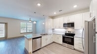 Located in Grand Prairie, TX, this 1-bedroom, 1-bathroom unit offers a thoughtfully designed single-floor layout with modern finishes throughout. The open-concept kitchen and living area serves as the heart of the space, featuring white shaker cabinetry, a subway tile backsplash, granite countertops with a peninsula island, and a full suite of stainless steel appliances including a refrigerator with ice maker, electric range, microwave, and dishwasher. Pendant lighting and recessed fixtures illuminate the kitchen, while a ceiling fan and large window bring natural light into the adjoining living area. Light wood-style flooring extends throughout the main living spaces, complementing the warm, neutral color palette. The living room opens to the outdoors via French doors and an additional window, offering views of the surrounding neighborhood. The bedroom is carpeted and features a window with blinds, providing a quiet and comfortable retreat. A dedicated closet offers ample storage. The bathroom includes a full tub-shower combination with tile surround. The entrance area houses a practical in-unit washer closet with built-in shelving. The property also includes access to a fenced outdoor green space.