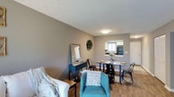 Located at 2845 Palumbo Dr in Lexington, Kentucky, this single-story space offers a practical and well-organized open-concept layout that seamlessly connects the main living areas. The living room provides a comfortable, welcoming atmosphere with warm hardwood-style flooring that carries throughout the space, neutral gray walls, and a textured ceiling that adds subtle visual interest. A cozy seating arrangement anchors the living area, which flows naturally into a dedicated dining space featuring a compact table with industrial-style metal chairs — ideal for casual dining or gathering. A decorative console table with a mirror adds a refined touch to the transitional space. A pass-through window connects the dining area directly to the kitchen, enhancing the open feel while maintaining a sense of organization between spaces. The kitchen, visible through the pass-through, features white cabinetry and modern appliances. Flush-mount ceiling lighting provides consistent illumination throughout. The overall ambiance is clean, modern, and functional, with thoughtful design choices that maximize the utility of the layout while maintaining a cohesive and inviting aesthetic throughout.
