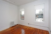 This single-floor unit combines classic architectural character with modern updates throughout. Rich, warm-toned hardwood floors run continuously across the main living areas and bedroom, lending a timeless quality to the space. The open main living area is defined by clean white walls, exposed ceiling beams, and multiple windows that invite natural light and frame views of the surrounding urban streetscape.

The kitchen is efficiently laid out with white cabinetry extending to the ceiling, marble-look quartz countertops, a stainless steel undermount sink, and a full suite of stainless steel appliances including a gas range, over-the-range microwave, and dishwasher. A tall stainless steel refrigerator is positioned conveniently at the kitchen's edge.

The bedroom benefits from dual windows offering elevated city views, with hardwood floors continuing throughout and perimeter baseboard heating ensuring year-round comfort. The bathroom is finished with full-height white subway tile surrounding the bathtub and shower, a wall-mounted sink with a mirrored medicine cabinet above, and a classic patterned mosaic tile floor that adds a vintage aesthetic detail. The overall ambiance of the unit is clean, bright, and functional, blending period character with contemporary finishes.