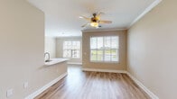 Located at 195 N Creek Dr in Summerville, South Carolina, this single-story residence offers a thoughtfully designed, open-concept layout with a warm, neutral color palette throughout. The living and dining area is filled with natural light from multiple large windows dressed with white blinds, and features wood-look laminate flooring and a ceiling fan with light fixture. Crown molding adds a refined touch to the main living spaces. The kitchen is well-appointed with dark cabinetry, light stone countertops, stainless steel appliances including a refrigerator, range, and microwave, and flows seamlessly into the dining area. A door from the kitchen area provides direct outdoor access. The bedrooms are carpeted for comfort and include ceiling fans, generous closet space with built-in rods, and windows that bring in natural light. The bathroom features a full tub-shower combo with built-in shelving, wood-look tile flooring, and clean white fixtures. Throughout the home, wide baseboards and consistent finishes create a cohesive aesthetic. Outdoor views of the surrounding greenery and neighborhood are visible from multiple rooms, enhancing the overall sense of openness and connection to the natural surroundings.