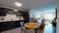 Located in Manor, TX, this single-floor unit offers a well-designed, functional layout with consistent wood-look flooring flowing throughout the main living areas. The open-concept living room is bright and welcoming, featuring a ceiling fan, a window fitted with blinds that allows natural light to fill the space, and a floor vent for climate control. The living area connects seamlessly to the kitchen, creating an efficient and cohesive common area.

The kitchen is well-appointed with dark espresso cabinetry offering ample storage, light granite-style countertops, and a full suite of black appliances including a refrigerator, electric range with overhead microwave, and dishwasher. A double-basin sink completes the kitchen's practical setup.

The entryway provides a welcoming transition into the unit, with easy access to a closet and the hallway leading to the other rooms. The bedroom is a quiet, neutral-toned space with wood-look flooring and panel-style doors. The bathroom features light tile flooring, a tub-shower combination, a vanity with dark cabinetry, and clean white walls that contribute to a bright, crisp atmosphere. The overall design is clean and modern, with neutral tones and practical finishes throughout.