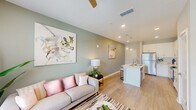 This well-appointed single-floor residence offers a thoughtfully designed open-concept layout that seamlessly connects the kitchen, dining, and living areas. The kitchen is a standout feature, outfitted with crisp white shaker cabinetry, light quartz countertops, a classic subway tile backsplash, and a full suite of stainless steel appliances including a refrigerator, electric range, and over-the-range microwave. A central island with a double sink and bar seating serves as both a functional workspace and a casual gathering spot, illuminated by elegant pendant lighting overhead. Light wood-style flooring flows throughout the main living areas, lending warmth and continuity to the space. The living room is bright and inviting, featuring sage-green accent walls, large windows that welcome natural light, and a ceiling fan for added comfort. Two well-sized bedrooms offer plush carpeting and ceiling fans, with one room showcasing a bold teal accent wall and the other featuring dual windows that fill the space with light. The bathroom is finished with neutral tile surrounds, a tub-shower combination, and clean white vanity cabinetry. Throughout, the home strikes a balance between modern design and everyday functionality.