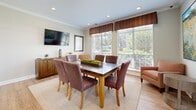 Situated at 1825 Grove Point Rd in Savannah, Georgia, this single-floor space is thoughtfully designed to balance functionality with a warm, welcoming ambiance. The interiors are finished with light hardwood flooring throughout, neutral wall tones, and crown molding that adds a refined architectural touch.

The dining area serves as a central gathering space, featuring a large wood-framed table surrounded by upholstered chairs in rich earthy tones. Oversized windows dressed with wood-valance window treatments and horizontal blinds flood the room with natural light while offering views of the surrounding greenery. A wall-mounted flat-screen TV and a wooden credenza provide additional utility, while curated artwork adds visual warmth. A cozy armchair and side table tucked into the corner offer a secondary seating option.

A dedicated workstation area provides a productive environment with a granite-topped desk accommodating dual computer monitors and a multifunction printer, supported by ergonomic task chairs. Decorative framed artwork hangs above the workspace, enhancing the professional yet comfortable atmosphere.

The entry features a classic French-style glass-paned door that invites natural light into the space and provides a pleasant view of the landscaped exterior. Together, these spaces create a cohesive, functional environment ideal for both collaborative and individual use.