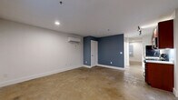 Located at 219 E Bank St in Petersburg, VA, this one-bedroom, one-bathroom unit offers an efficient and thoughtfully designed layout across a single floor. Polished concrete floors run throughout the space, lending an industrial yet modern character that ties the rooms together cohesively.

The open living area features crisp white walls accented by a bold slate-blue feature wall, recessed lighting, and a wall-mounted mini-split HVAC unit for individualized climate control. A window allows natural light to filter in, brightening the space.

The kitchen is well-equipped with rich cherry wood cabinetry reaching toward the ceiling for ample storage, a full suite of stainless steel appliances including a range, microwave, dishwasher, and refrigerator, white countertops, and track lighting overhead. An exposed wooden structural post adds a distinctive industrial-historic touch.

The bedroom is a comfortable size, featuring its own mini-split unit and a window with a blind for privacy. The bathroom is cleanly finished with classic penny-tile flooring, a warm wood-toned vanity, a toilet, and a walk-in shower with a clean white surround. Additional functionality is provided by a dedicated laundry area, a closet, and a utility room, making this a complete and practical living space.