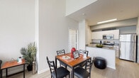 This two-floor residence offers a well-designed layout that balances functionality and comfort across its living spaces. The main level features an open-concept arrangement where the living room, dining area, and kitchen flow seamlessly together. The living room stands out with impressively tall ceilings that amplify the sense of space, light wood-style flooring, and windows that invite natural light. A dedicated dining area sits adjacent to the kitchen, accommodating a four-seat table beneath the generous vertical space created by the double-height ceiling.

The kitchen is thoughtfully designed in a galley-style configuration, featuring white cabinetry with sleek hardware, gray quartz-style countertops, a matte black sink faucet, tile backsplash, and a full suite of stainless steel appliances including a refrigerator, range, and built-in microwave.

The two bedrooms are carpeted for warmth and comfort, each equipped with a ceiling fan and windows fitted with blinds that offer natural light and privacy. The upper-level bedroom features a vaulted ceiling, adding an airy feel to the space.

Both bathrooms share a consistent, clean aesthetic with white cabinetry, gray countertops, and tub-shower combinations with curtained enclosures, complemented by light wood-style flooring throughout.