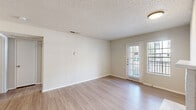 This well-appointed one-bedroom, one-bathroom single-floor unit offers a thoughtfully designed layout across a comfortable footprint. The open living room is highlighted by light wood-look flooring, a textured ceiling, and a charming white brick fireplace flanked by built-in shelving. A glass door floods the space with natural light and provides exterior access. The layout flows seamlessly from the living area through a hallway into the galley-style kitchen, which is equipped with stainless steel appliances including a range, over-the-range microwave, and refrigerator, complemented by gray cabinetry with modern hardware, light countertops, and track lighting overhead. A convenient pass-through connects the kitchen to the living area. The bedroom features soft carpeting, a ceiling fan with integrated lighting, a window with outdoor views, and direct access to a dedicated walk-in closet with built-in shelving. The bathroom is finished with a gray vanity, a framed mirror with dark hardware accents, a full tub-shower combination, and light wood-look flooring consistent with the rest of the unit. A hallway connects all areas efficiently, completing this clean, move-in-ready layout.