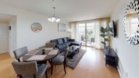 This single-floor residence is thoughtfully designed with a cohesive nautical theme carried throughout its interiors. The open-concept living and dining area serves as the heart of the home, featuring light hardwood flooring, a large sectional sofa accented with blue patterned throw pillows, and a dining set beneath a chandelier. Sheer curtains frame sliding glass doors that open to a private balcony, allowing natural light to fill the space. Nautical artwork, including sailboat paintings and a ship's wheel clock, reinforces the coastal aesthetic throughout.

The kitchen is well-appointed with warm-toned wood cabinetry, granite countertops, light hardwood flooring, and a full suite of stainless steel appliances, including a gas range, microwave, and refrigerator. Under-cabinet lighting adds a functional and polished touch.

The bedroom is carpeted and serene, furnished with a rich cherry wood sleigh bed, matching nightstands, and a full-length mirror. A large window allows ample natural light. Two bathrooms feature large-format tile flooring, warm wood vanities with granite countertops, and glass-enclosed shower options—one with a standalone shower and one with a combination tub and shower.