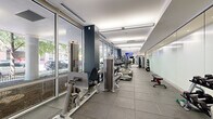 Located in Chicago's vibrant West Loop neighborhood, this fitness center at 922 W Washington Blvd offers a comprehensive workout facility within a thoughtfully designed, elongated space. The layout is defined by a wall of floor-to-ceiling windows along one side, flooding the interior with natural light and providing open views of the surrounding streetscape. Durable rubber-tiled flooring runs throughout, providing both safety and functionality underfoot.

The cardio zone is well-equipped with a row of Matrix treadmills, elliptical trainers, and stationary bikes, all positioned to take advantage of the natural light and exterior views. A wall-mounted flat-screen TV adds an entertainment option for users during workouts. Transitioning deeper into the space, a dedicated strength training area features a multi-station cable machine, adjustable benches, and a full rack of dumbbells organized along mirrored and frosted glass walls.

Functional training is supported by a tiered medicine ball rack stocked with various weights, kettlebells, and additional free weights. The frosted glass partition walls lend a clean, modern aesthetic while enhancing the sense of openness. Recessed and linear overhead lighting ensures consistent illumination throughout. The overall design is sleek and contemporary, reflecting the modern architectural character of the West Loop area.