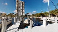 This waterfront property offers a compelling combination of tropical surroundings and direct marina access, making it a notable option for boating enthusiasts. The exterior of the building presents a clean, modern architectural profile characterized by wide horizontal lines, large windows, and an open façade that integrates well with its verdant setting. Mature palm trees and well-maintained tropical hedging frame the structure, lending it a serene, resort-like atmosphere.

The property's standout exterior feature is its private boat slip, numbered and positioned along a well-maintained white dock that sits directly on calm waterway waters. The marina setting provides open views across the water, with lush greenery and a striking high-rise tower visible in the background, underscoring the prime waterfront location.

The surrounding landscaping is carefully curated, with dense tropical foliage, manicured shrubs, and towering palms creating a sense of privacy and natural beauty. The single-story layout suggests easy accessibility throughout the space. While interior images were not sufficiently clear to detail specific room features, the overall setting conveys a relaxed, Florida waterfront lifestyle defined by its outdoor amenities, direct water access, and tropical ambiance.