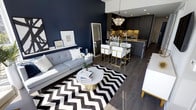 This single-floor space showcases a thoughtfully designed open-concept layout that seamlessly integrates the living and kitchen areas into one cohesive environment. The living area commands attention with a dramatic navy blue feature wall, which serves as a striking backdrop to a contemporary grey tufted sofa adorned with crisp white cushions. A bold black-and-white chevron area rug anchors the seating zone, complemented by a round marble-topped coffee table with a brushed gold base that adds a refined, glamorous touch.

The kitchen and dining area flow naturally from the living space, featuring dark wood cabinetry paired with granite countertops that lend a rich, moody contrast. A stunning crystal chandelier hangs above the dining area, casting warm light over white upholstered dining chairs with gold-toned frames — a detail that reinforces the space's elegant aesthetic. Recessed ceiling lighting further brightens the kitchen zone.

Dark hardwood flooring runs throughout, unifying the areas with warmth and continuity. The overall ambiance is modern and luxurious, defined by a confident interplay of deep navy, crisp white, rich wood tones, and gleaming gold accents.