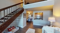 Located at 2700 Village Green Dr in Aurora, IL, this two-story residence offers a well-designed layout that balances open communal spaces with comfortable private retreats. The main level immediately impresses with a double-height living area, where a staircase with dark wood treads and wrought iron balusters rises dramatically alongside the open floor plan. Dark hardwood-style flooring flows through the living and dining areas, creating a cohesive and polished aesthetic. A pass-through window connects the dining space to the galley-style kitchen, which features rich warm-toned cabinetry, dark granite countertops, a mosaic tile backsplash, and stainless steel appliances. A sitting nook with large windows offering greenery views adds a bright, inviting corner to the main level.

Upstairs, the second floor provides a loft-style landing that overlooks the living area below. Multiple bedrooms are carpeted for comfort, each offering ample natural light through sizable windows. The primary bedroom includes a closet and dedicated dresser space, while a second bedroom comfortably accommodates additional sleeping arrangements. Two full bathrooms serve the residence, each finished with warm wood vanities, white countertops, tile-accented tub-shower combinations, and wood-look flooring. A dedicated office or flex space with hardwood-style floors and ceiling fan completes the upper level.