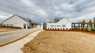 Camellia Grove is a freshly constructed residential development in Lafayette, LA, showcasing a blend of contemporary design and community-focused features. The entrance is marked by a distinctive white wall bearing the community's name and logo, welcoming residents and visitors alike. The development comprises a variety of housing styles, including single-story and two-story structures with clean, modern lines and neutral color palettes.

The community's infrastructure is well-planned, with paved roads, sidewalks, and ample parking areas, including visitor spots near the entrance. Landscaping is in its early stages, with young trees planted throughout, promising future shade and greenery. A notable feature is the communal area, which includes a pergola-covered space strung with lights, suggesting a place for gatherings and social events.

Camellia Grove also boasts practical amenities, such as a large bank of mailboxes centrally located for convenience. The development appears to be built with an eye towards open spaces, with grassy areas interspersed between housing units and roads. Street lighting is provided for safety and ambiance during evening hours. The overall atmosphere is one of a fresh start, with the potential for a close-knit community as the development matures and residents make it their home.