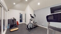Located at 524 Venice Way in Inglewood, CA, this single-floor fitness studio is thoughtfully designed to support a comprehensive workout experience. The main workout area features striking vaulted ceilings with recessed lighting that enhance the sense of openness and volume throughout the space. Durable rubber flooring covers the entire workout zone, providing safety and comfort during exercise. The room is equipped with cardio machines including a NordicTrack treadmill and an elliptical trainer, along with free weights, medicine balls, resistance equipment, and various training accessories organized along the walls. A wall-mounted mini-split HVAC unit ensures year-round climate control. Large floor-to-ceiling glass sliding doors connect the main workout area to a secondary training room, which features a putting green mat and additional equipment, creating a seamless and versatile multi-zone fitness environment. Frosted glass interior doors add privacy while maintaining a bright, airy atmosphere. The studio also includes a functional restroom fitted with a vanity, mirror cabinet, and commercial-grade soap and paper towel dispensers, reflecting the space's professional character. The clean white walls and modern finishes throughout contribute to a focused, motivating environment well-suited for personal or professional fitness use.