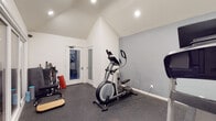 Located at 524 Venice Way in Inglewood, CA, this single-floor fitness studio is thoughtfully designed to support a comprehensive workout experience. The main workout area features striking vaulted ceilings with recessed lighting that enhance the sense of openness and volume throughout the space. Durable rubber flooring covers the entire workout zone, providing safety and comfort during exercise. The room is equipped with cardio machines including a NordicTrack treadmill and an elliptical trainer, along with free weights, medicine balls, resistance equipment, and various training accessories organized along the walls. A wall-mounted mini-split HVAC unit ensures year-round climate control. Large floor-to-ceiling glass sliding doors connect the main workout area to a secondary training room, which features a putting green mat and additional equipment, creating a seamless and versatile multi-zone fitness environment. Frosted glass interior doors add privacy while maintaining a bright, airy atmosphere. The studio also includes a functional restroom fitted with a vanity, mirror cabinet, and commercial-grade soap and paper towel dispensers, reflecting the space's professional character. The clean white walls and modern finishes throughout contribute to a focused, motivating environment well-suited for personal or professional fitness use.