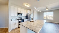 This well-appointed single-floor residence offers a thoughtfully designed open-concept layout that seamlessly connects the kitchen, dining, and living areas. The kitchen serves as the centerpiece of the space, showcasing a large granite-topped island with an undermount sink, white shaker cabinetry, stone countertops, and a full suite of stainless steel appliances including a range, microwave, and refrigerator. A sleek pendant light above the island adds a modern touch. The living area is generously proportioned, featuring light hardwood-style flooring and an abundance of natural light streaming through multiple windows. Sliding glass doors open to a private balcony, offering pleasant outdoor views that bring the outside in. The bedroom is carpeted for comfort and includes a ceiling fan and a window with views of the surrounding area. The bathrooms are finished with granite-topped vanities, white cabinetry, and wood-look tile flooring. Accessibility-friendly features are present throughout, including grab bars in the shower and tub areas. The tub surround features clean white subway-style tile. A neutral color palette and contemporary finishes create a cohesive, modern ambiance throughout the entire space.