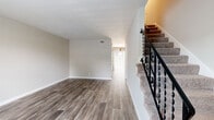 This two-story residence offers a thoughtfully designed layout that balances comfort and modern style throughout its two levels. The main floor greets visitors with warm, wood-style plank flooring that flows through the open living and dining areas, complemented by neutral-toned walls and clean white baseboards. A standout pendant light fixture anchors the dining area, while large vertical blinds allow for generous natural light. The hallway connects to the rear of the home, where natural light filters in from an exterior-facing window or door.

The kitchen is a true highlight, featuring a two-tone cabinet design with crisp white upper cabinets adorned with gold hardware and dark lower cabinets. A deep farmhouse sink, dark granite countertops, a bold dark subway tile backsplash, a skylight, and a full suite of stainless steel appliances complete this well-equipped space.

An elegant staircase with ornate wrought iron railings and plush carpeted treads leads to the upper level, where the bedrooms are finished with soft wall-to-wall carpet and ceiling fans. Each bedroom benefits from natural light through window blinds. The bathroom is clean and modern, featuring a white vanity with dark stone countertops, a round mirror, and a shower-tub combination.
