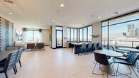 Located along West Colfax Avenue in Denver, Colorado, this contemporary single-floor amenity space offers a sophisticated and open layout designed for both relaxation and social gathering. The interior is unified by light-toned hardwood-style flooring and crisp white ceilings with recessed lighting, creating a bright and airy atmosphere throughout.

Floor-to-ceiling windows and black-framed glass walls line multiple sides of the space, flooding the interior with natural light and showcasing sweeping panoramic views of the Denver skyline and the Rocky Mountains. A set of sliding glass doors provides seamless access to an expansive outdoor terrace, extending the usable space and enhancing the connection to the outdoors.

The lounge area anchors one end of the space, centered around a sleek linear fireplace set within a light wood-paneled surround, above which a large-format television is mounted. A generous sectional sofa and curated accent pieces contribute to the area's inviting, residential feel. An eye-catching geometric chevron accent wall in blue and white tones adds a bold design statement near the dining nook, which features built-in banquette seating beneath a modern pendant light fixture.

A dark-toned kitchen island with bar seating serves as a functional centerpiece for the space, complemented by additional bistro-style seating arrangements positioned to take full advantage of the city views. The overall design balances modern aesthetics with comfort, making this a well-appointed communal destination.