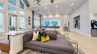 Located at 2307 Ridgemont Ave in Charlotte, NC, this single-floor community living space offers an impressive and welcoming atmosphere defined by its dramatic vaulted ceilings adorned with rustic exposed wood beams and an elegant modern chandelier. Light hardwood flooring flows throughout, complementing the crisp white walls and soft neutral tones that give the space a bright, airy character.

The open floor plan is thoughtfully divided into distinct functional zones. At the entrance, a stylish reception and lounge area features contemporary seating, curated wall art, and a built-in coffee and beverage station, setting a refined first impression. A blue accent wall with integrated display features adds a bold design focal point near the entry lounge.

Further into the space, a generous seating area centered around a large sectional sofa and a dual-screen media wall provides a comfortable gathering spot. A full-size billiards table anchors an adjacent recreation zone, ideal for social interaction. Floor-to-ceiling windows along the far wall flood the interior with natural light and offer views of the surrounding exterior, enhancing the sense of openness. A dining area with white-topped tables and coordinating chairs completes the layout, making this a fully equipped and versatile communal amenity space.