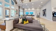 Located at 2307 Ridgemont Ave in Charlotte, NC, this single-floor community living space offers an impressive and welcoming atmosphere defined by its dramatic vaulted ceilings adorned with rustic exposed wood beams and an elegant modern chandelier. Light hardwood flooring flows throughout, complementing the crisp white walls and soft neutral tones that give the space a bright, airy character.

The open floor plan is thoughtfully divided into distinct functional zones. At the entrance, a stylish reception and lounge area features contemporary seating, curated wall art, and a built-in coffee and beverage station, setting a refined first impression. A blue accent wall with integrated display features adds a bold design focal point near the entry lounge.

Further into the space, a generous seating area centered around a large sectional sofa and a dual-screen media wall provides a comfortable gathering spot. A full-size billiards table anchors an adjacent recreation zone, ideal for social interaction. Floor-to-ceiling windows along the far wall flood the interior with natural light and offer views of the surrounding exterior, enhancing the sense of openness. A dining area with white-topped tables and coordinating chairs completes the layout, making this a fully equipped and versatile communal amenity space.