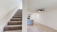 Located at 7049 Westwind Dr in El Paso, TX, this two-story residence offers a thoughtfully designed layout spread across two floors. The main level features an open-concept living room and kitchen area, where light wood-look flooring and neutral tones create a clean, contemporary atmosphere. A striking stone-tile accent wall frames a fireplace in the living room, serving as a bold focal point alongside a large window that invites natural light. A ceiling fan adds comfort and style overhead. The kitchen is well-appointed with gray shaker cabinetry, quartz countertops, stainless steel appliances including a refrigerator, electric range, microwave, and dishwasher, all illuminated by a skylight. A carpeted staircase leads to the upper level, where the generously sized primary bedroom features light wood flooring, a ceiling fan, and direct access to a private en-suite bathroom. A second full bathroom on the lower level includes a clean white vanity with a large mirror and a tub-shower combination. Textured walls throughout add architectural character, while ample closet space and two bathrooms enhance everyday functionality in this efficiently designed home.