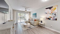 This thoughtfully designed 2-bedroom, 2-bathroom residence offers a comfortable and functional single-floor layout. The open-concept living and dining area serves as the heart of the home, featuring wood-look flooring, a textured ceiling, and a ceiling fan. A sliding glass door fills the space with natural light and provides direct access to a private patio overlooking a lushly landscaped outdoor area. The kitchen is efficiently appointed with white shaker-style cabinetry, white countertops, and a full suite of stainless steel appliances including a range, microwave, and refrigerator. A breakfast bar with seating for three connects the kitchen to the living area, making it ideal for casual dining. The primary bedroom offers a generous footprint with a ceiling fan, large window with natural light, and a walk-in closet. The second bedroom provides comparable comfort and versatility. Both bathrooms feature wood-look flooring, white vanities, and a tub-shower combination. A hallway connects the bedrooms and bathrooms, contributing to an efficient and private layout. Throughout the residence, neutral tones, consistent flooring, and clean lines create a cohesive, contemporary ambiance.