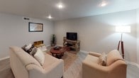 This single-floor residence offers a thoughtfully designed layout with consistent light gray walls, light wood-tone laminate flooring, and textured ceilings throughout. The living room provides a welcoming atmosphere, featuring recessed lighting, neutral-toned seating, and a front entry with window blinds that allow natural light to filter in.

The kitchen is efficiently arranged in a galley-style configuration, showcasing granite countertops, gray cabinetry, a mosaic tile backsplash, and an electric range. It opens directly into a dedicated dining area, which is illuminated by a pendant light fixture and comfortably accommodates a round four-seat dining set. A decorative mirror on the wall adds depth to the space.

The bedroom is a restful retreat equipped with a ceiling fan, a window with blinds, and ample room for a full furniture arrangement including a dresser with vanity mirror. The bathroom features a full tub-shower combination with white tile surround, a gray vanity with a speckled countertop, and wood-tone flooring that ties the space together. Throughout, the residence maintains a cohesive, neutral palette that conveys a clean and practical aesthetic.