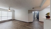 This single-floor residential unit offers a well-organized layout designed for comfortable everyday living. Throughout the space, rich dark hardwood-style flooring provides a cohesive and contemporary aesthetic, complemented by neutral-toned walls and dark baseboards.

The open living area is spacious and airy, featuring a ceiling fan with integrated lighting and a large window fitted with horizontal blinds that allow natural light to filter in. A hallway connects the main living space to the private quarters, lined with dark-trimmed doors that add a modern contrast to the neutral palette.

The kitchen is thoughtfully designed with gray cabinetry, white countertops, and stainless steel appliances including a range, over-the-range microwave, and refrigerator. A peninsula counter separates the kitchen from the adjacent dining or living area, providing both workspace and a casual dining option.

The bedrooms are generously proportioned, each equipped with a ceiling fan and windows that bring in natural light. The textured ceilings are consistent throughout the unit.

Two full bathrooms serve the space, each featuring a tub and shower combination, gray vanity cabinetry with white countertops, and matching hardwood-style flooring. The bathrooms are clean, functional, and finished with brushed nickel hardware and fixtures.