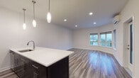 Located at 36 Pine St in Poughkeepsie, NY, this modern single-floor unit offers a thoughtfully designed open-concept layout with contemporary finishes throughout. The kitchen is a standout feature, equipped with dark cabinetry, stainless steel appliances including a refrigerator, range, and microwave, and a sleek white quartz peninsula countertop with an integrated sink. Elegant pendant lighting hangs above the peninsula, adding both function and style to the space. The kitchen flows seamlessly into a generously sized living area, where large windows invite abundant natural light and frame views of the surrounding Poughkeepsie neighborhood and distant landscape. Wood-look luxury vinyl plank flooring runs consistently throughout the main living spaces, lending a warm, cohesive aesthetic. A dedicated bedroom area benefits from corner windows that maximize light and provide additional outdoor views, along with a wall-mounted split-system air conditioning unit for climate control. The bathroom features neutral tile flooring, a tiled tub-shower combination, and clean white fixtures. Adjacent to the bathroom, a dedicated in-unit laundry closet houses a stacked washer and dryer, offering added convenience. The overall design is clean, modern, and move-in ready, with a neutral color palette that complements a variety of interior styles.