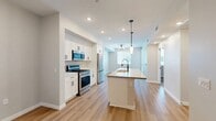 This thoughtfully designed single-story home in Redlands, California offers a comfortable and modern living experience across a well-utilized floor plan. The open-concept main living area seamlessly combines the kitchen, dining room, and living room into a bright, cohesive space. The kitchen is a standout feature, showcasing crisp white shaker cabinetry, a large center island with a built-in sink and pendant lighting overhead, stainless steel appliances including a gas range, microwave, and refrigerator, and light wood-tone luxury vinyl plank flooring that extends throughout the main areas. Recessed lighting enhances the clean, airy feel. The living area is bathed in natural light from a glass-paneled door that leads to a private patio. The bedroom offers plush carpeting, a window with blinds, and access to a spacious walk-in closet with built-in shelving and hanging rods for ample storage. The full bathroom features a tub/shower combination with white tile surround, a white vanity with quartz countertop, a large mirror, and sleek matte black fixtures throughout. A dedicated laundry area adds further convenience to this move-in-ready home.