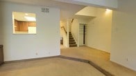 This two-story residence offers a straightforward and functional layout designed for comfortable everyday living. The main level greets visitors with a generously sized living area finished in neutral-toned carpet throughout, creating a warm and cohesive feel across the space. A notable architectural detail is the subtle split-level step within the living area, which adds dimension and visual interest to the open floor plan. Crisp white walls and a textured ceiling reflect light effectively, keeping the space feeling bright and airy. A central staircase, accented with wooden railings, serves as the natural focal point of the main level, providing a clean transition to the upper floor. Built-in shelving is visible near the staircase area, offering practical storage solutions. HVAC vents are integrated into the ceiling, ensuring climate control throughout the home. The open sightlines between areas of the main floor allow for a connected and spacious feel. The upper level, accessible via the carpeted staircase, extends the living space further. Overall, the home presents a clean, move-in ready canvas with a neutral palette and practical design elements suited to a variety of living arrangements.