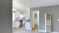 This single-floor, two-bedroom, one-bathroom unit offers a thoughtfully updated interior with a cohesive modern aesthetic. Light wood-tone vinyl flooring runs throughout the space, complementing the neutral gray and white color palette that gives the unit a clean, contemporary feel.

The kitchen is a standout feature, equipped with stainless steel appliances including a gas range, over-the-range microwave, refrigerator, and dishwasher. White shaker-style cabinetry with sleek hardware pairs with dark countertops and a subway tile backsplash, offering both style and functionality. A peninsula provides additional counter space and separates the kitchen from the adjoining living area.

The living room is bright and open, with natural light filtering through horizontal blinds. A wall-mounted air conditioning unit provides climate control, and the open layout allows for flexible furniture arrangements.

Both bedrooms are comfortably sized, each featuring natural light from windows with outdoor views of surrounding greenery. One bedroom includes a closet with sliding mirror doors and track lighting overhead.

The bathroom features marble-look tile in the shower and on the floor, a wide dark-topped vanity with an undermount sink, a round mirror, and brushed nickel fixtures, creating a refined and polished finish.