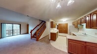 This two-story residence is designed with a practical and comfortable layout spread across both levels. The main level centers around an open living area finished with neutral carpeting, anchored by a staircase with a warm oak wood railing that leads to the upper floor. A decorative chandelier illuminates the entry area, where two solid wood doors provide access points. The kitchen is well-appointed with abundant oak cabinetry, open shelving, light countertops, and white appliances including a range, refrigerator, and dishwasher. Tile flooring defines the kitchen zone, transitioning cleanly from the carpeted living space.

Upstairs, a carpeted hallway loft area overlooks the staircase via a classic oak balustrade, adding an open, airy quality to the upper level. Bedrooms feature carpet flooring and windows that frame wooded outdoor views, with one room offering sliding glass door access to a balcony. A secondary bathroom includes an oak vanity, extended countertop, and a large mirror. The spacious primary bathroom is a standout feature, offering a dual-sink vanity, a corner jetted soaking tub, and a separate shower, all finished with light flooring for a bright, clean aesthetic.