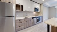 Located at 20 George St in downtown Hamilton, Ontario, this modern 2-bedroom, 1-bathroom unit offers a well-designed layout with contemporary finishes throughout. Light wood-tone flooring runs seamlessly across the entire space, complementing the neutral grey and warm beige tones on the walls, creating a bright and cohesive aesthetic.

The kitchen is a standout feature, showcasing two-tone cabinetry with wood-grain lower cabinets and gloss white upper cabinets, paired with a crisp white countertop, subway tile backsplash, and a full suite of stainless steel appliances including an oven, dishwasher, and built-in microwave. The adjacent living and dining area benefits from large floor-to-ceiling windows and direct access to a private balcony, offering expansive city views.

Both bedrooms are bright and well-proportioned, each featuring windows with roller blinds that frame elevated views of the Hamilton skyline. The primary bedroom includes a full-wall built-in wardrobe with wood-panel doors and matte black hardware, providing generous storage.

The bathroom is finished with a wood-grain vanity, white countertop, framed mirror, and a glass-enclosed walk-in shower, maintaining the clean modern aesthetic found throughout the unit.