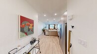 Located at 6741 Boulder Hwy in Las Vegas, NV, this efficiently designed one-bedroom, one-bathroom residence offers a thoughtful open-concept floor plan that maximizes every square foot. Light wood-style flooring flows seamlessly throughout the space, creating a cohesive and airy aesthetic.

The kitchen is a standout feature, equipped with stainless steel appliances including a refrigerator with ice maker, electric range, over-the-range microwave, and dishwasher. Flat-front light wood cabinetry extends to the ceiling for ample storage, while the white countertops and peninsula layout make the kitchen ideal for both cooking and casual dining. Pendant lighting above the peninsula adds a modern touch, and the open sightlines connect the kitchen directly to the living area, which benefits from natural light through a large window.

The bedroom is a comfortable retreat featuring a ceiling fan, a natural light-filled window with curtains, and a soft blue accent wall. An adjacent closet provides dedicated storage.

The bathroom is clean and functional, offering a full soaking tub and shower combination with tiled surround, built-in open shelving for linens, and warm, neutral finishes. The entry area provides additional functional space, completing this well-appointed Las Vegas residence.