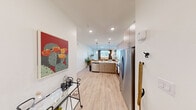 Located at 6741 Boulder Hwy in Las Vegas, NV, this efficiently designed one-bedroom, one-bathroom residence offers a thoughtful open-concept floor plan that maximizes every square foot. Light wood-style flooring flows seamlessly throughout the space, creating a cohesive and airy aesthetic.

The kitchen is a standout feature, equipped with stainless steel appliances including a refrigerator with ice maker, electric range, over-the-range microwave, and dishwasher. Flat-front light wood cabinetry extends to the ceiling for ample storage, while the white countertops and peninsula layout make the kitchen ideal for both cooking and casual dining. Pendant lighting above the peninsula adds a modern touch, and the open sightlines connect the kitchen directly to the living area, which benefits from natural light through a large window.

The bedroom is a comfortable retreat featuring a ceiling fan, a natural light-filled window with curtains, and a soft blue accent wall. An adjacent closet provides dedicated storage.

The bathroom is clean and functional, offering a full soaking tub and shower combination with tiled surround, built-in open shelving for linens, and warm, neutral finishes. The entry area provides additional functional space, completing this well-appointed Las Vegas residence.