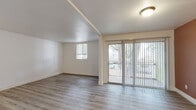 This single-floor residence is designed with a clean, neutral aesthetic throughout. Light wood-style flooring runs continuously across all living areas, creating a cohesive and modern feel. The main living area is bright and open, benefiting from a large sliding glass door that opens onto a private balcony, offering views of surrounding trees and the outdoor environment. Vertical blinds frame the glass door, allowing for adjustable light control, while an additional window further enhances natural light in the space.

A separate bedroom features its own window with a view of the outdoors, white walls, and the same consistent wood-style flooring. A standout room includes a bold terracotta accent wall that adds warmth and character, contrasting with the otherwise neutral palette. An additional room, visible in the floor plan, provides flexible space.

The galley-style kitchen is efficiently laid out with white cabinetry, light countertops, a stainless steel sink, and black appliances including a refrigerator, electric range, and dishwasher. A recessed ceiling detail adds subtle architectural interest overhead.

The bathroom features a full-size soaking tub with an integrated shower surround, chrome fixtures, and a curtain rod, maintaining the unit's clean, functional design throughout.