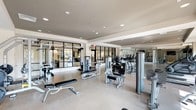 Located at 260 Leigh Farm Rd in Durham, NC, this professionally equipped fitness center offers a spacious, single-floor layout designed to accommodate a wide range of workout needs. The facility is bathed in natural light streaming through large floor-to-ceiling windows along the perimeter, complemented by recessed ceiling lighting that ensures a bright, energizing environment throughout.

The space is organized into distinct functional zones. A dedicated strength training area houses an extensive selection of selectorized resistance machines, free weight benches, and a full dumbbell rack, all set against floor-to-ceiling mirrors that enhance the sense of depth. Glass-panel partitions divide sections of the facility while maintaining an open, airy feel.

The cardio zone features a long row of treadmills, stationary bikes — including upright and recumbent models — ellipticals, and stair climbers, many equipped with integrated screens. Wall-mounted televisions are positioned throughout for entertainment during workouts. A functional training area includes a TRX suspension training rig, medicine balls, and balance equipment set on light hardwood-style flooring, ideal for dynamic and circuit-based training.

The overall aesthetic is modern and clean, with neutral tones, durable flooring, and a well-organized layout that supports both individual and group fitness routines. Outdoor views through the windows add a welcoming ambiance to the entire space.
