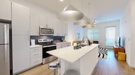 Located at 2125 E Apache Blvd in Tempe, Arizona, this thoughtfully designed one-bedroom, one-bathroom unit maximizes every inch of its well-organized floor plan. The open-concept kitchen and living area serves as the heart of the home, anchored by a striking white waterfall island with bar seating and an undermount sink. The kitchen features white cabinetry, stainless steel appliances including a refrigerator, electric range, and over-the-range microwave, all complemented by a bold navy blue subway tile backsplash. Three large statement pendant lights hang above the island, adding a modern, design-forward touch. Light wood-style flooring flows throughout the entire unit, creating a warm and cohesive aesthetic. The living area benefits from multiple windows and a glass-panel door that invites natural light and provides outdoor access. The bedroom is a calm retreat with large windows, ample natural light, and a dedicated closet with built-in shelving. The full bathroom features a clean white vanity, wood-look flooring, and a tub/shower combination. A convenient in-unit stacked washer and dryer is tucked neatly near the entryway, maximizing functionality within the space.