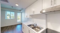 Located at 4212 Genesee Ave in San Diego, CA, this single-floor unit offers a thoughtfully designed layout comprising a living room, kitchen, bathroom, and hallway. Throughout the space, warm wood-look flooring and crisp white walls create a clean, contemporary aesthetic that maximizes the sense of openness.

The living room is bright and airy, featuring large windows fitted with horizontal blinds that invite natural light while maintaining privacy. The minimalist design allows for flexible furniture arrangements, and the neutral palette provides a versatile backdrop for any décor style.

The kitchen is efficiently laid out with white cabinetry offering ample storage above and below the counter. A double-basin stainless steel sink sits alongside a smooth-top electric range and oven, complemented by an overhead ventilation hood. Light stone-finish countertops and sleek hardware reinforce the modern, functional character of the space.

The bathroom continues the clean design language, featuring wood-look flooring, a white vanity with under-sink cabinetry, a large wall mirror, and recessed lighting overhead. The layout is practical and well-proportioned.

A connecting hallway ties the rooms together seamlessly, contributing to the unit's efficient flow. Overall, this San Diego unit presents a well-maintained, modern interior suited for comfortable urban living.