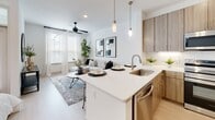 Located at 4830 N Shepherd Dr in Houston, TX, this single-story unit presents a cohesive modern aesthetic defined by bright white walls, light wood-tone flooring, and an open-concept layout that encourages seamless flow between living areas. The kitchen serves as a central hub, outfitted with warm wood-grain cabinetry extending floor to ceiling, stainless steel appliances including a refrigerator, range, and built-in microwave, plus white quartz countertops and a subway tile backsplash. A peninsula with pendant lighting above doubles as a dining surface, connecting the kitchen directly to the living area. The living space is generously proportioned, featuring large windows with full-length curtains that draw in natural light and a ceiling fan for added comfort. The bedroom is bright and tranquil, benefiting from additional windows and direct visual openness to the main living zone. A hallway with recessed lighting and a paneled door leads further into the unit. The bathroom is cleanly finished with marble-look tile flooring, a subway-tiled tub/shower combo, and wood-grain vanity cabinetry with a white quartz countertop. Throughout, the design maintains a consistent palette of warm neutrals and contemporary materials, resulting in a polished and functional living environment.