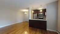 This single-floor residence offers a thoughtfully designed open-concept layout that seamlessly connects the kitchen, dining, and living areas. Rich hardwood flooring flows throughout, reflecting natural light and lending warmth to every room. The kitchen is a standout feature, showcasing dark espresso cabinetry, light countertops, a glass tile backsplash, and a full suite of stainless steel appliances including a gas range, microwave, refrigerator, and dishwasher. Pendant lighting above the peninsula adds a stylish focal point, while a large window over the sink invites natural light. The adjacent dining area is anchored by an elegant chandelier, and the open living space beyond features a wide window with outdoor views, creating an airy and connected feel. The bedrooms are generously sized with gleaming hardwood floors, ample closet space, and wall-unit climate control. The bathroom is finished with crisp white tile, decorative grey tile banding, a soaking tub, a modern vanity with stone countertop, and a bright frosted window. Throughout the residence, baseboard heating, clean neutral walls, and consistent flooring create a cohesive and comfortable living environment.